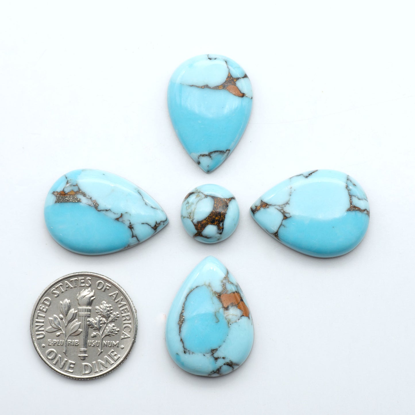Pressed Turquoise nugget cabochons, stabilized composite with blue color and dark matrix on a white background, with a US dime for scale.