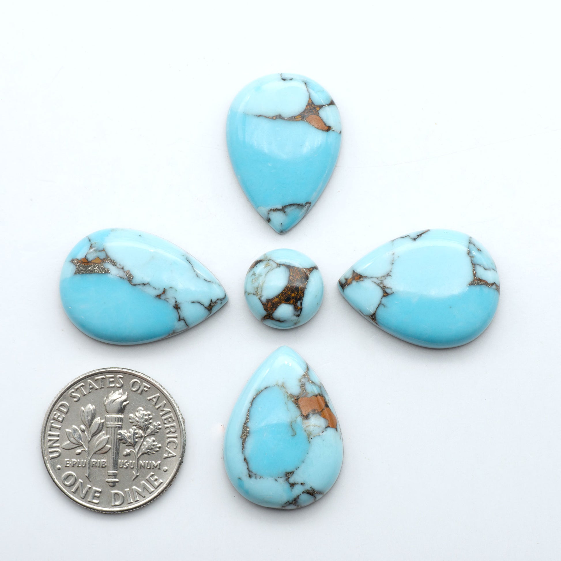 Pressed Turquoise nugget cabochons, stabilized composite with blue color and dark matrix on a white background, with a US dime for scale.