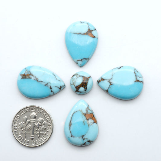 Pressed Turquoise nugget cabochons, stabilized composite with blue color and dark matrix on a white background, with a US dime for scale.