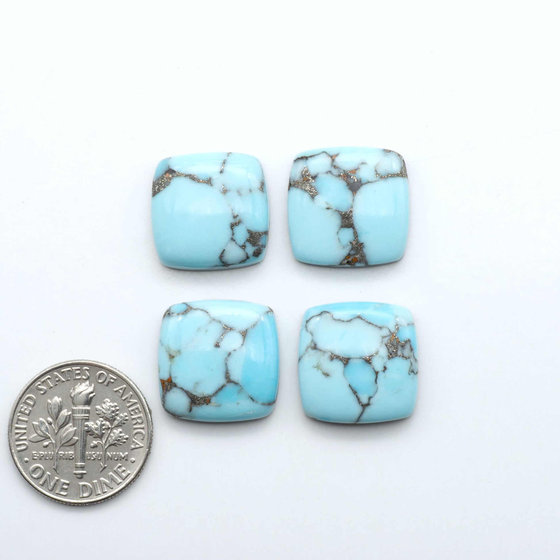 Pressed Turquoise nugget cabochons, stabilized composite with blue color and dark matrix on a white background, with a US dime for scale.