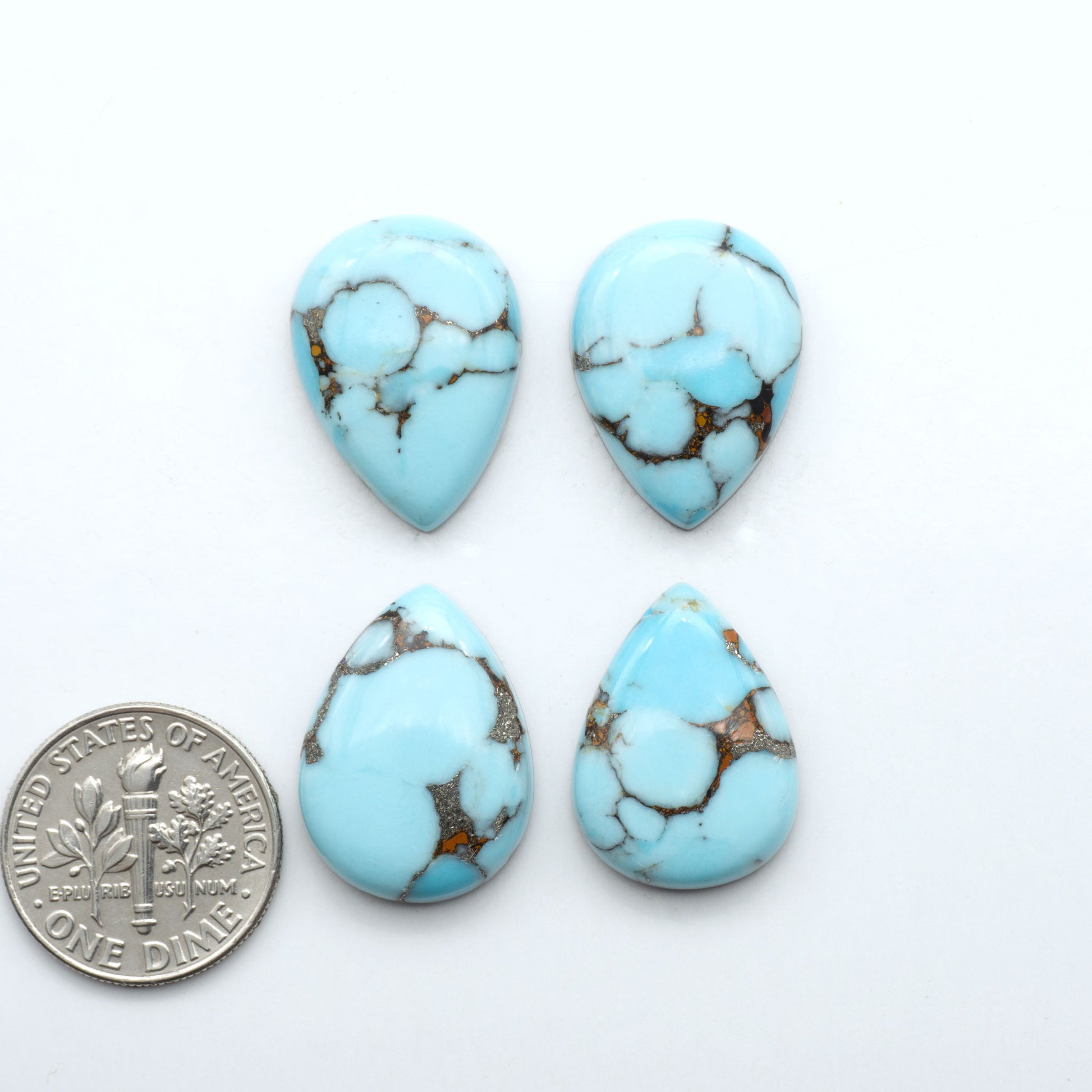 Pressed Turquoise nugget cabochons, stabilized composite with blue color and dark matrix on a white background, with a US dime for scale.