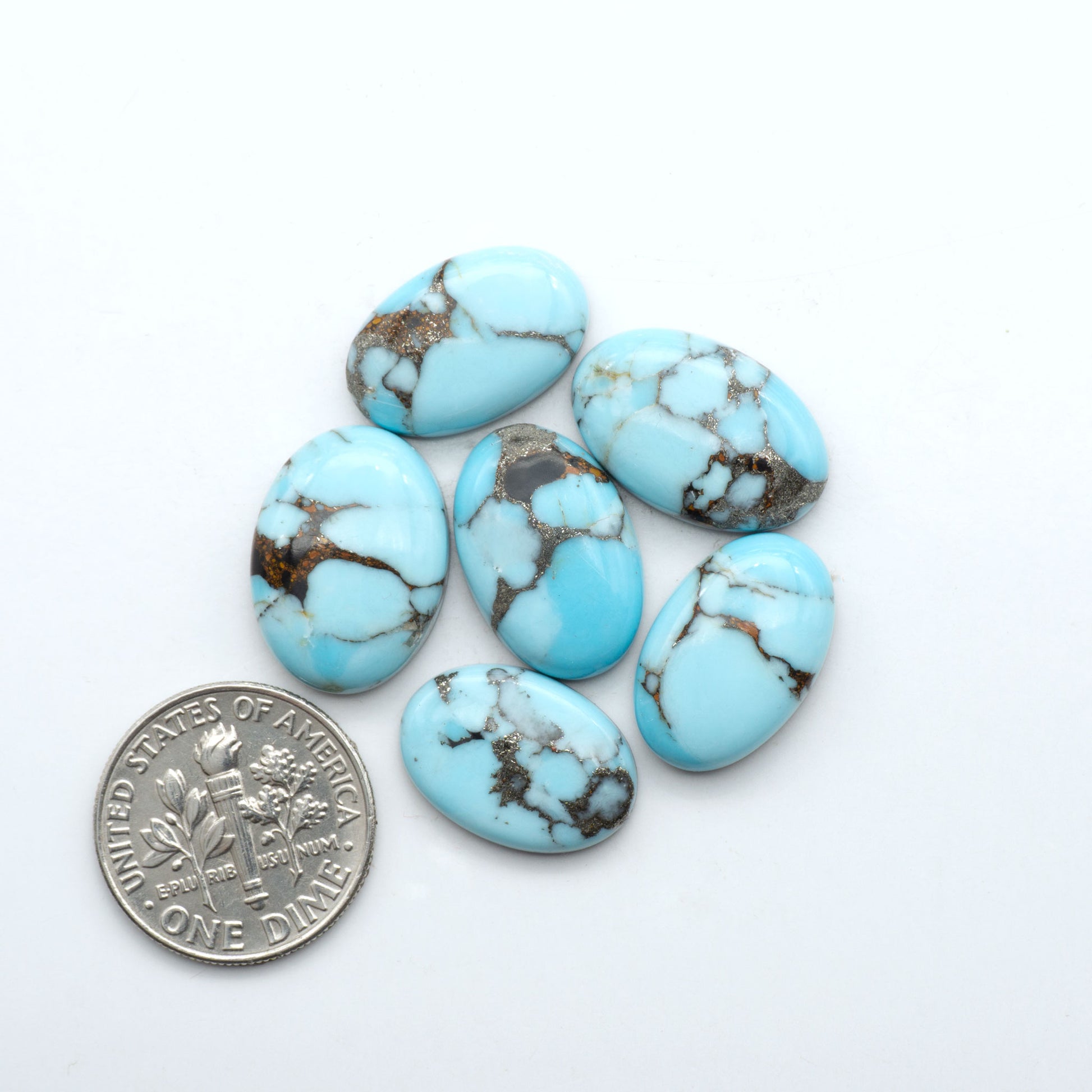 Pressed Turquoise nugget cabochons, stabilized composite with blue color and dark matrix on a white background, with a US dime for scale.