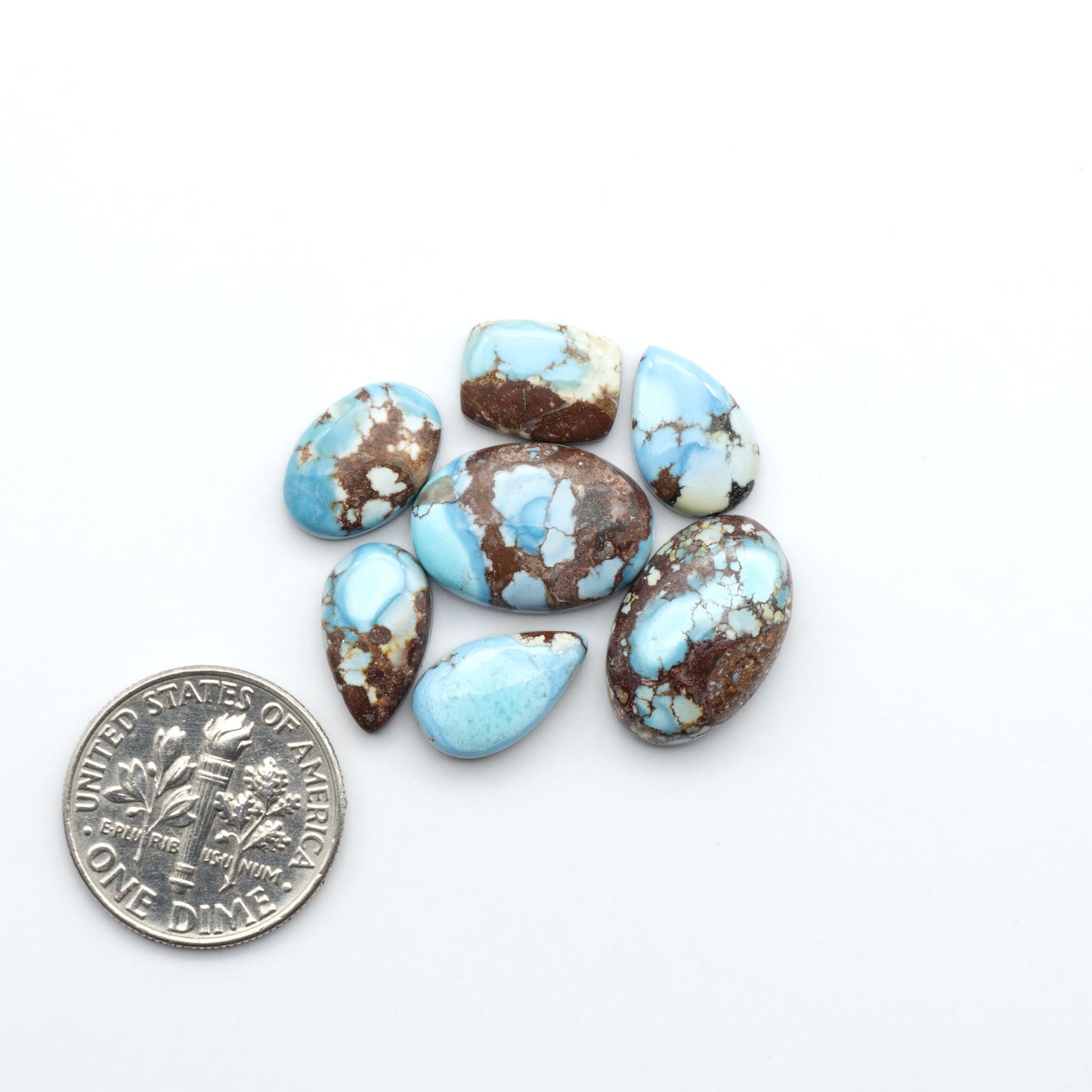Golden Hills Turquoise cabochons, icy blue to lavender tones with chocolate matrix, polished stones on a white background with a US dime for scale
