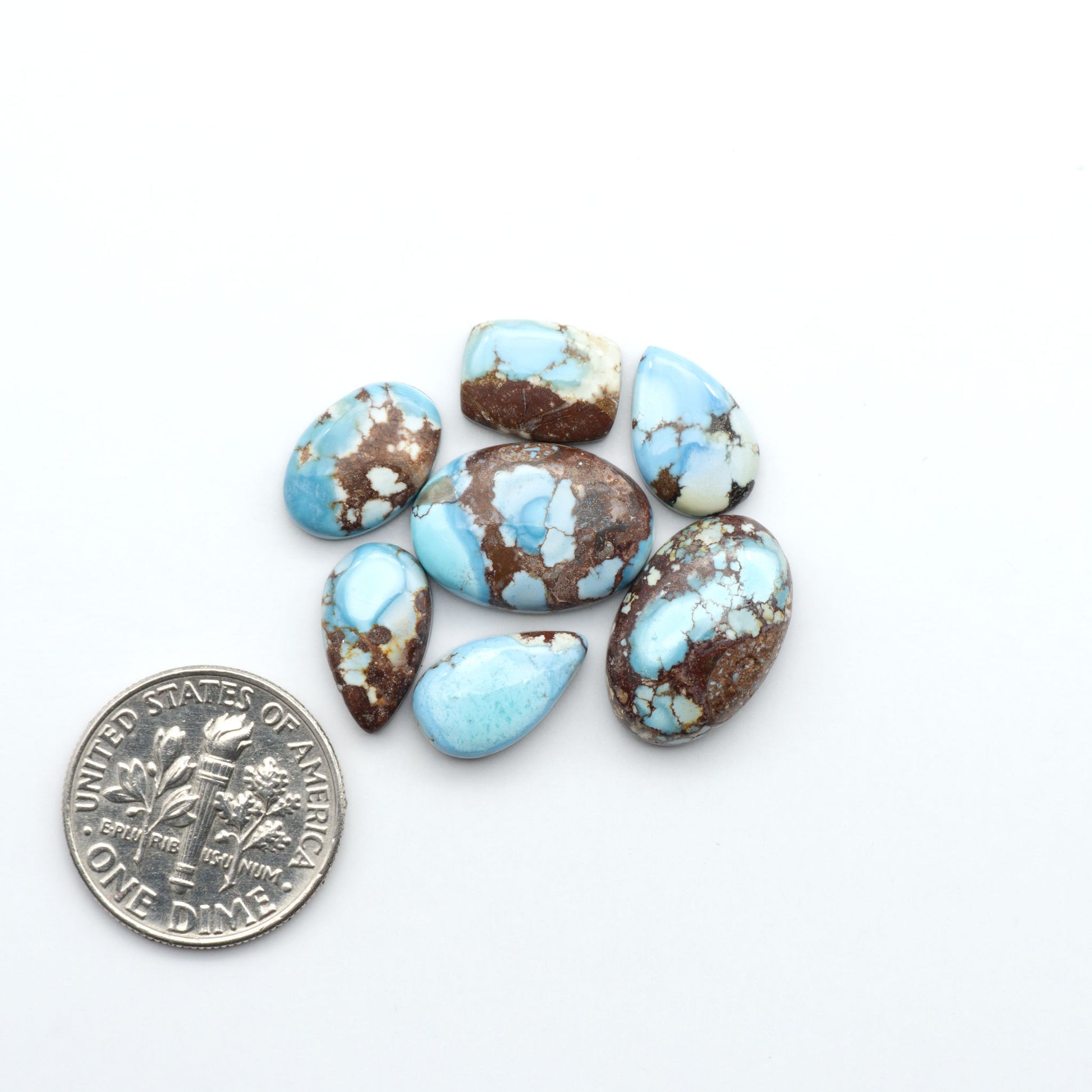 Golden Hills Turquoise cabochons, icy blue to lavender tones with chocolate matrix, polished stones on a white background with a US dime for scale