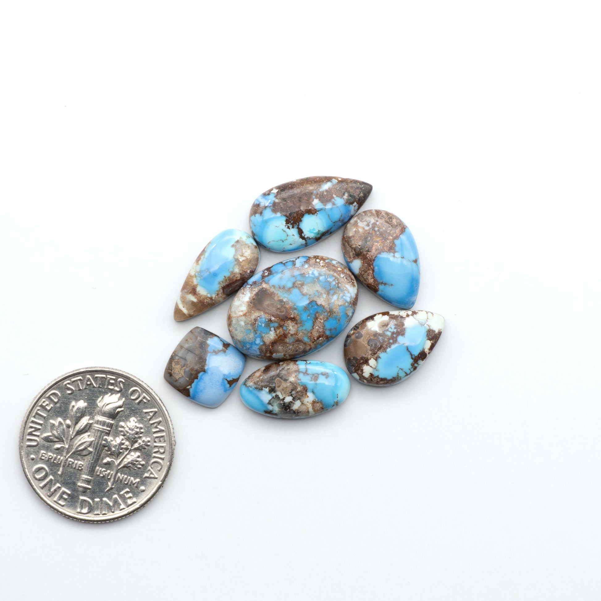 Golden Hills Turquoise cabochons, icy blue to lavender tones with chocolate matrix, polished stones on a white background with a US dime for scale