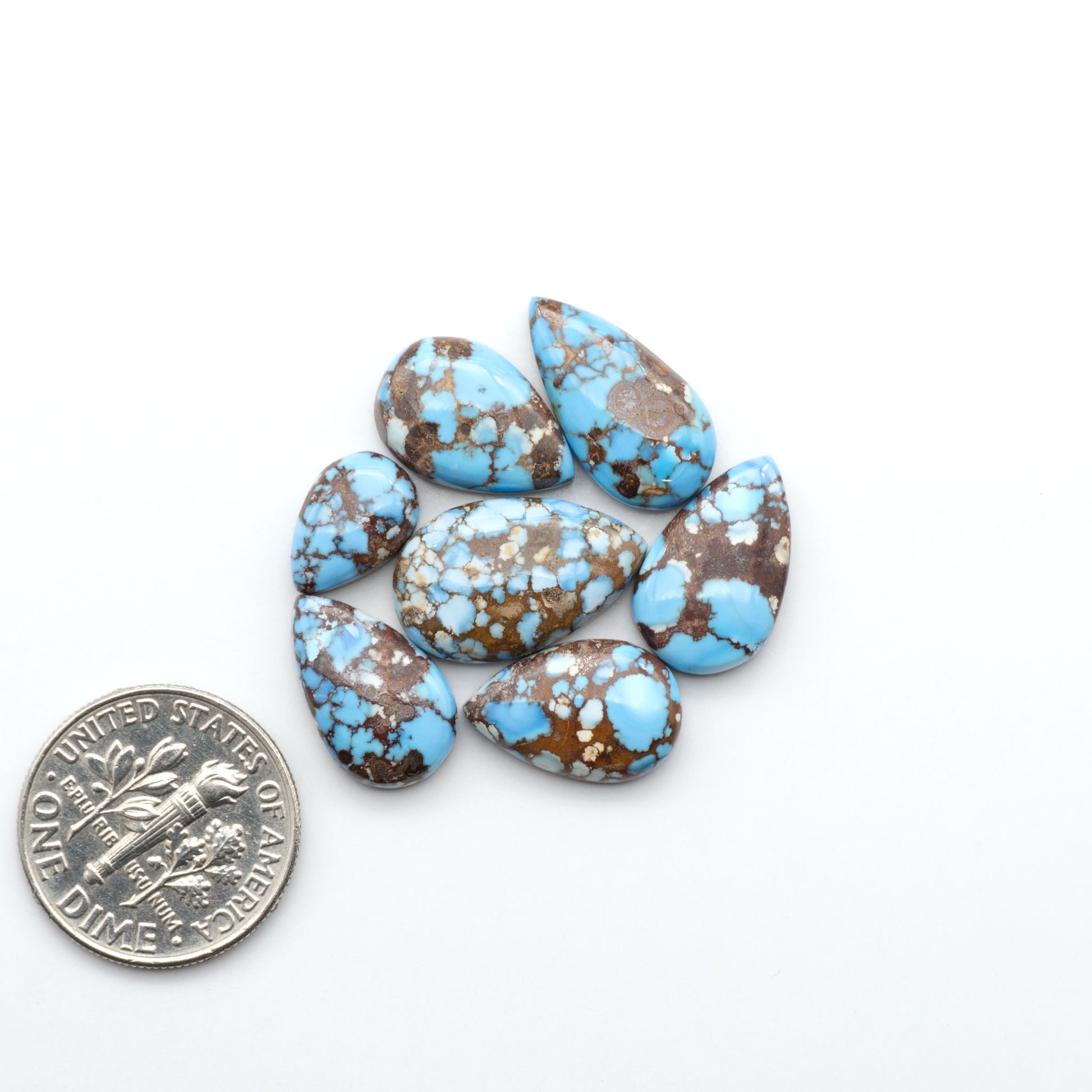 Golden Hills Turquoise cabochons, icy blue to lavender tones with chocolate matrix, polished stones on a white background with a US dime for scale