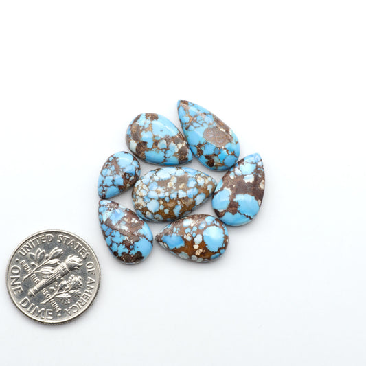 Golden Hills Turquoise cabochons, icy blue to lavender tones with chocolate matrix, polished stones on a white background with a US dime for scale