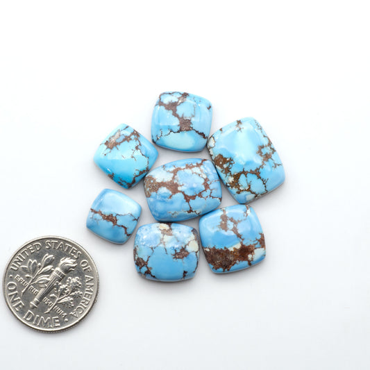 Golden Hills Turquoise cabochons, icy blue to lavender tones with chocolate matrix, polished stones on a white background with a US dime for scale