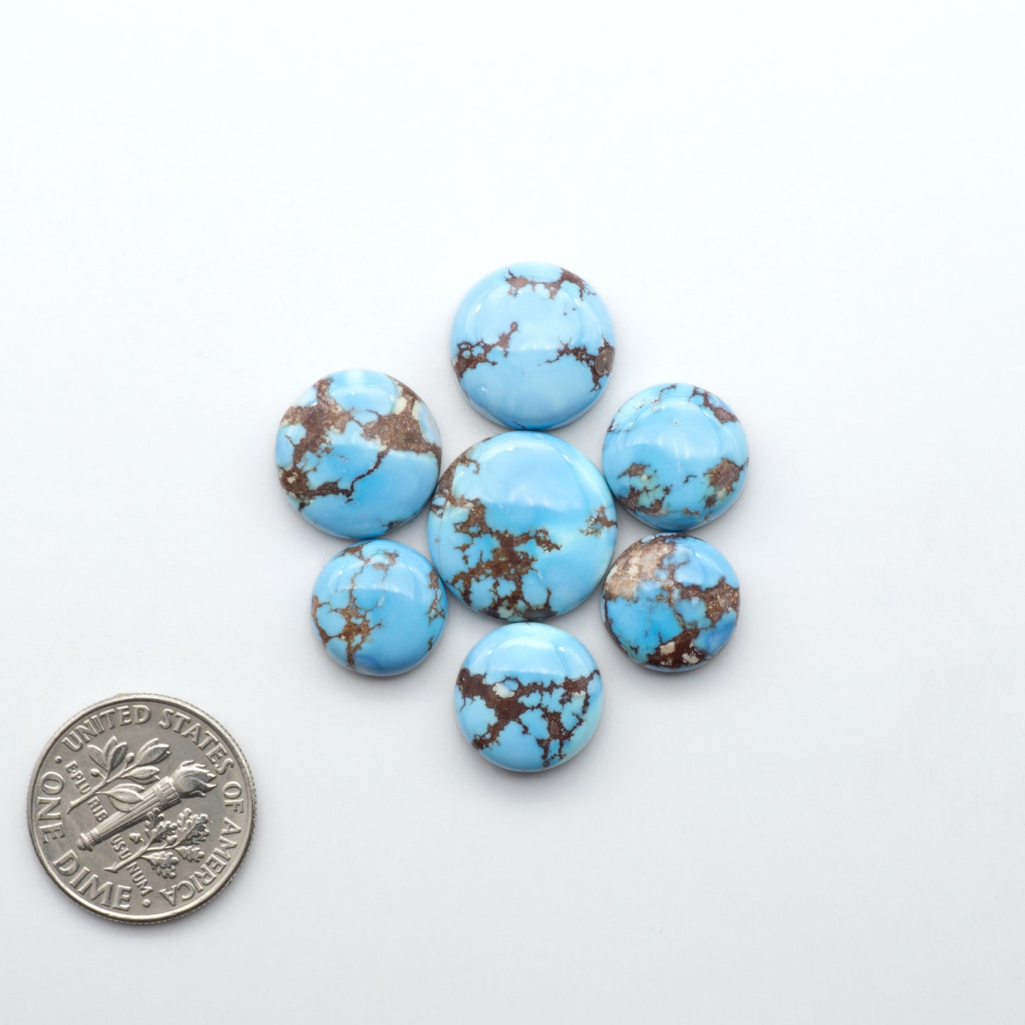 Golden Hills Turquoise cabochons, icy blue to lavender tones with chocolate matrix, polished stones on a white background with a US dime for scale