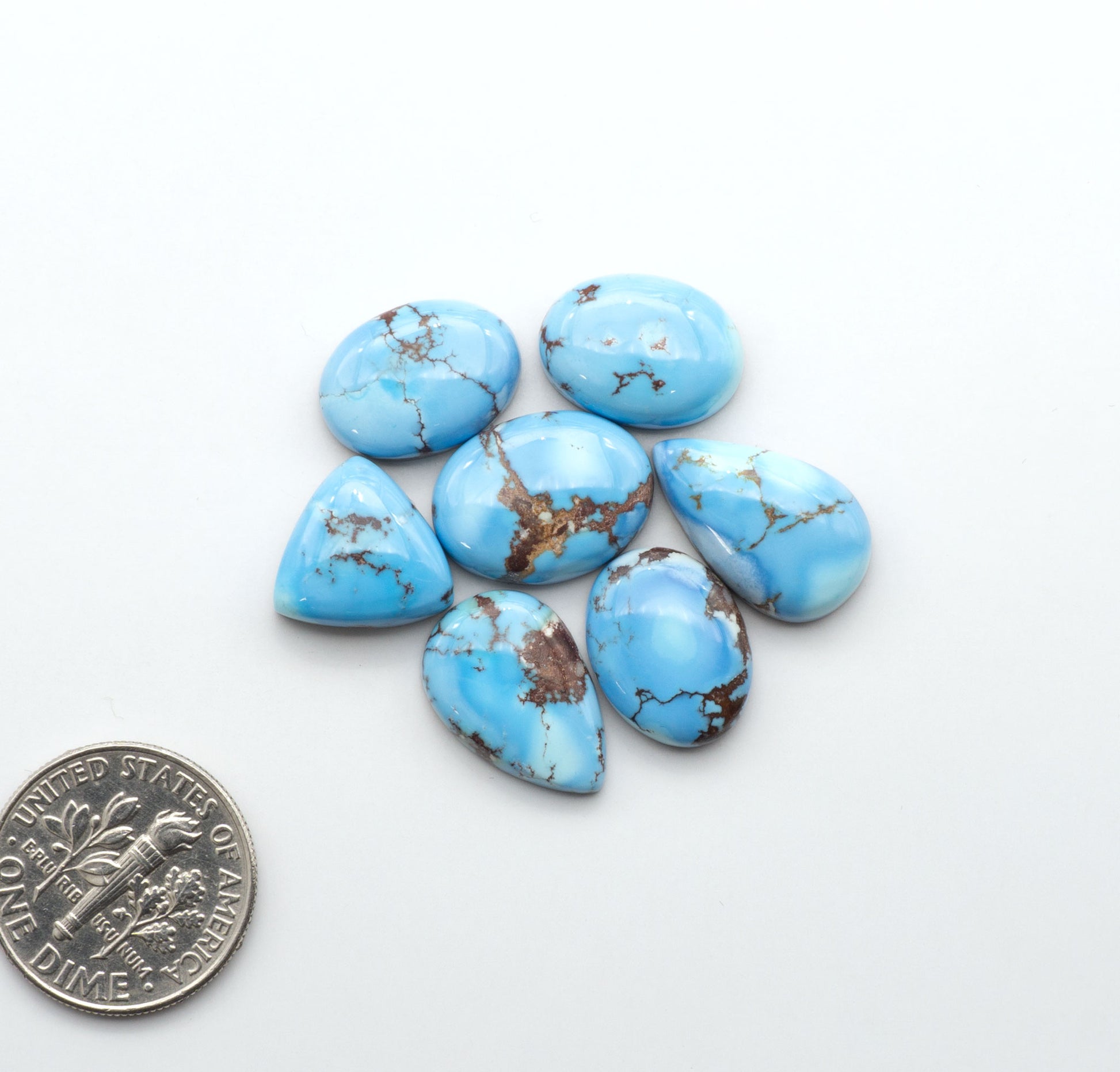 Golden Hills Turquoise cabochons, icy blue to lavender tones with chocolate matrix, polished stones on a white background with a US dime for scale