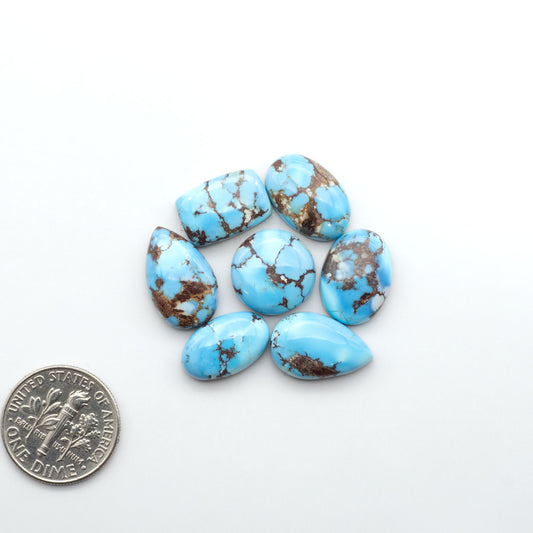 Golden Hills Turquoise cabochons, icy blue to lavender tones with chocolate matrix, polished stones on a white background with a US dime for scale