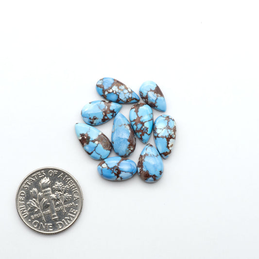 Golden Hills Turquoise cabochons, icy blue to lavender tones with chocolate matrix, polished stones on a white background with a US dime for scale