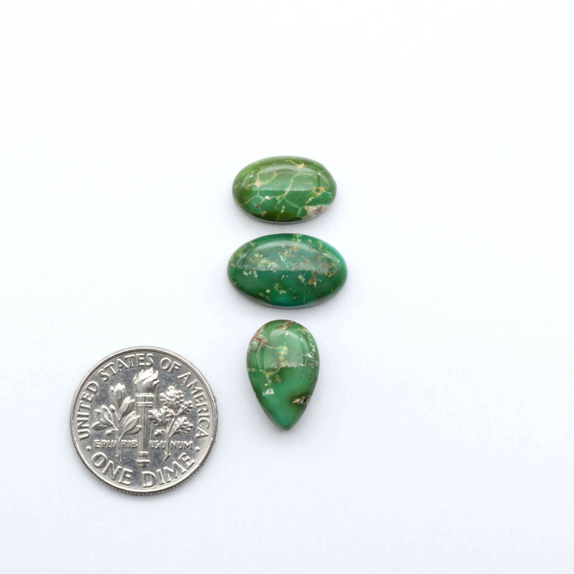 Sonoran Mountain Turquoise cabochons, blue-green color with natural matrix, polished stones on a white background, with a US dime for scale