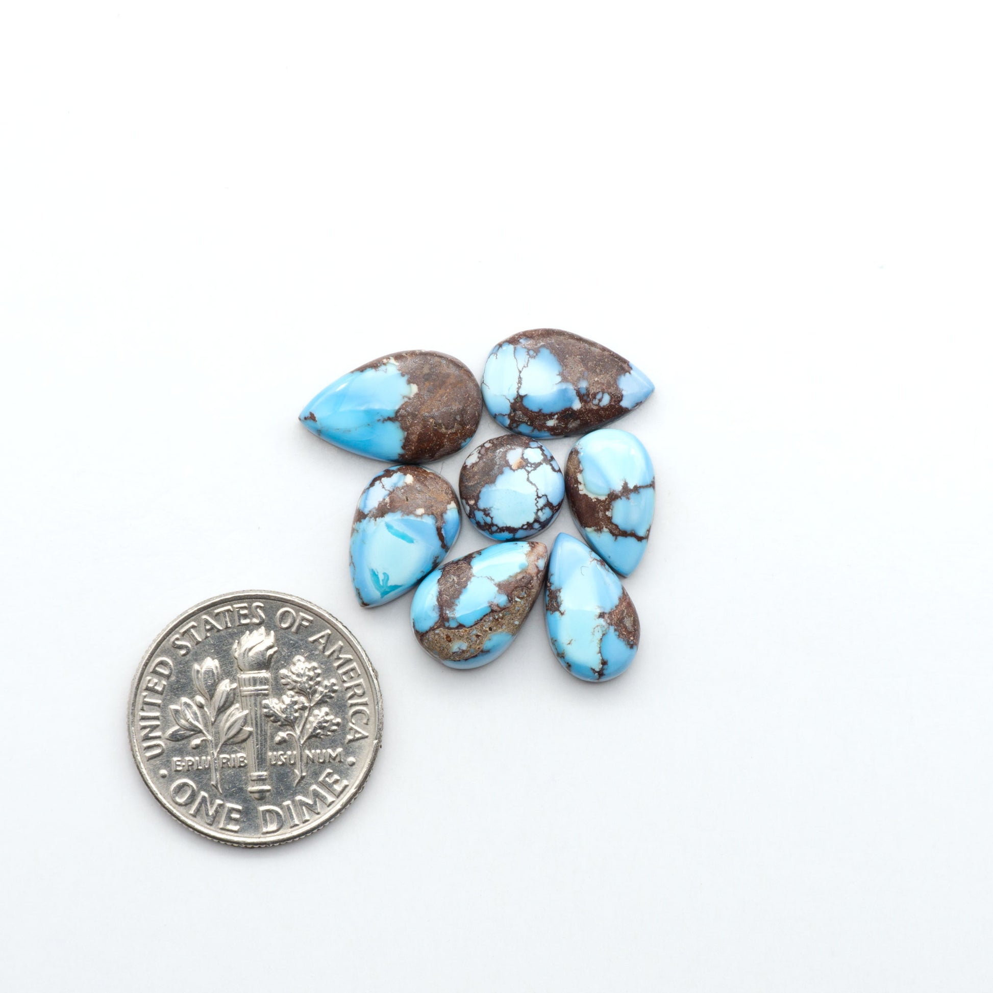 Golden Hills Turquoise cabochons, icy blue to lavender tones with chocolate matrix, polished stones on a white background with a US dime for scale
