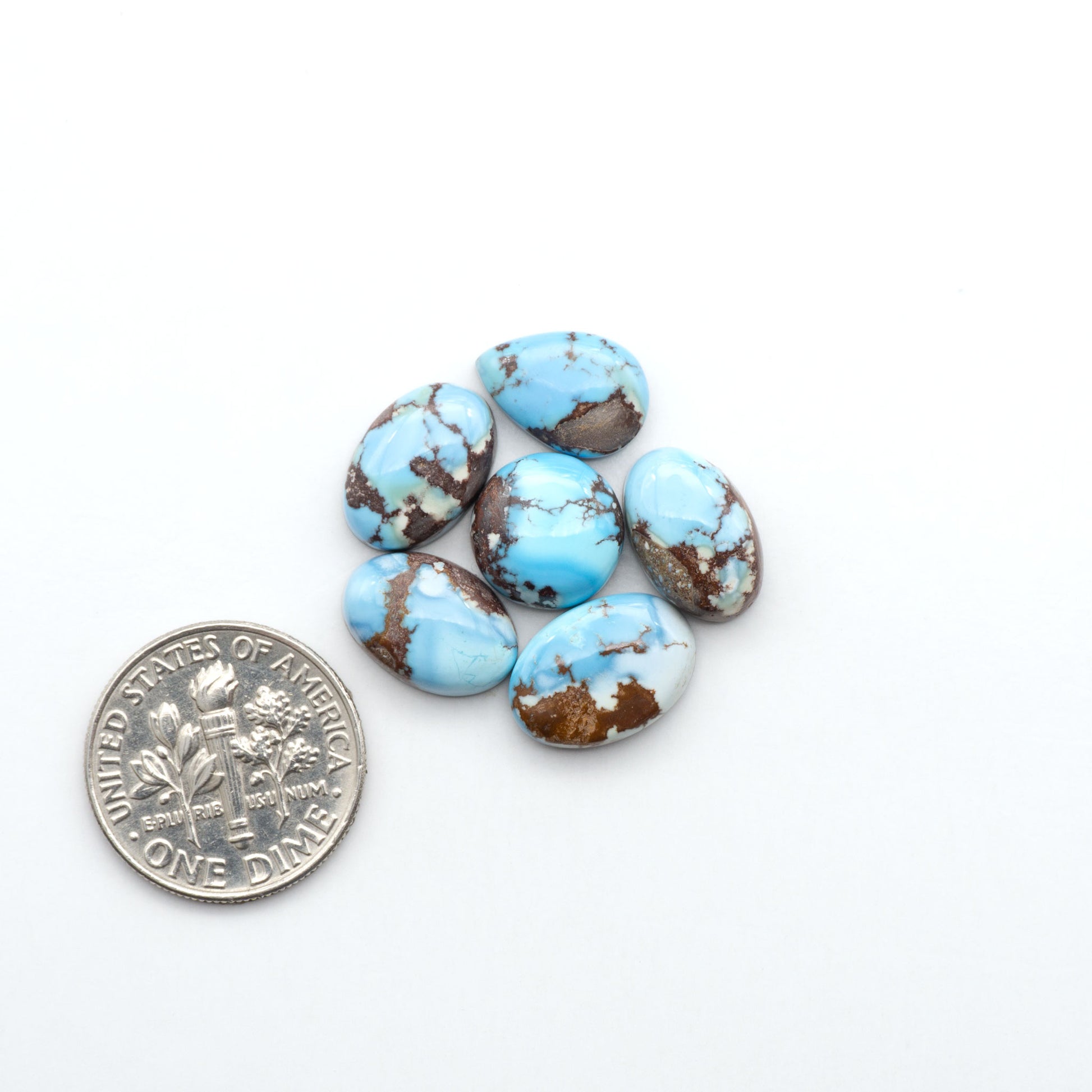 Golden Hills Turquoise cabochons, icy blue to lavender tones with chocolate matrix, polished stones on a white background with a US dime for scale