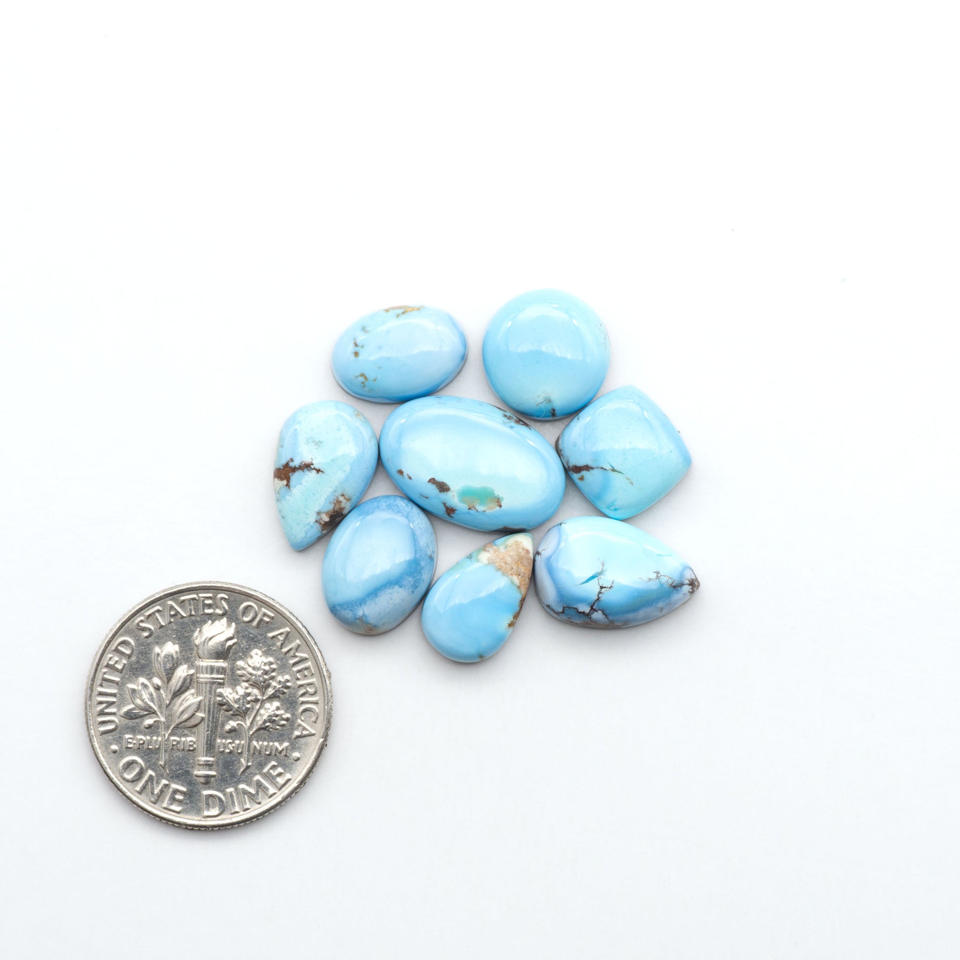 Golden Hills Turquoise cabochons, icy blue to lavender tones with chocolate matrix, polished stones on a white background with a US dime for scale