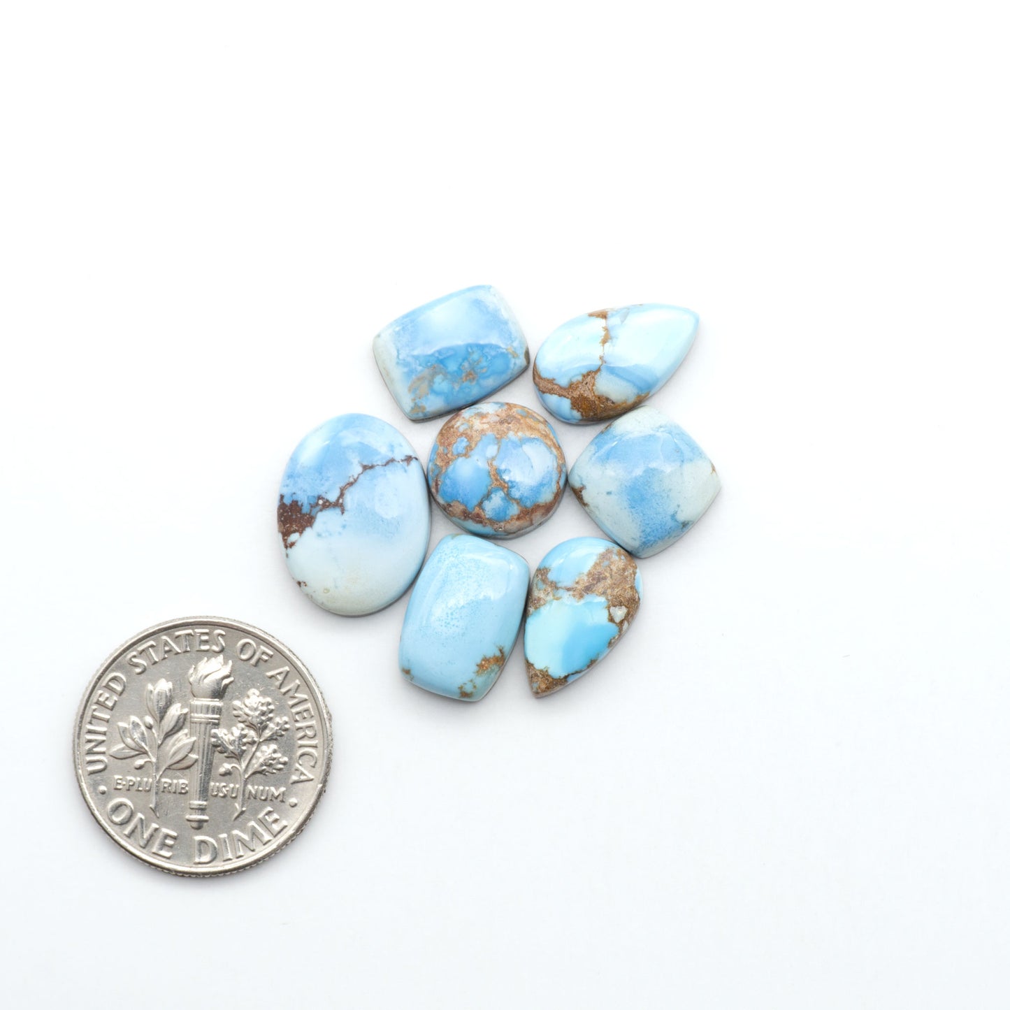 Golden Hills Turquoise cabochons, icy blue to lavender tones with chocolate matrix, polished stones on a white background with a US dime for scale