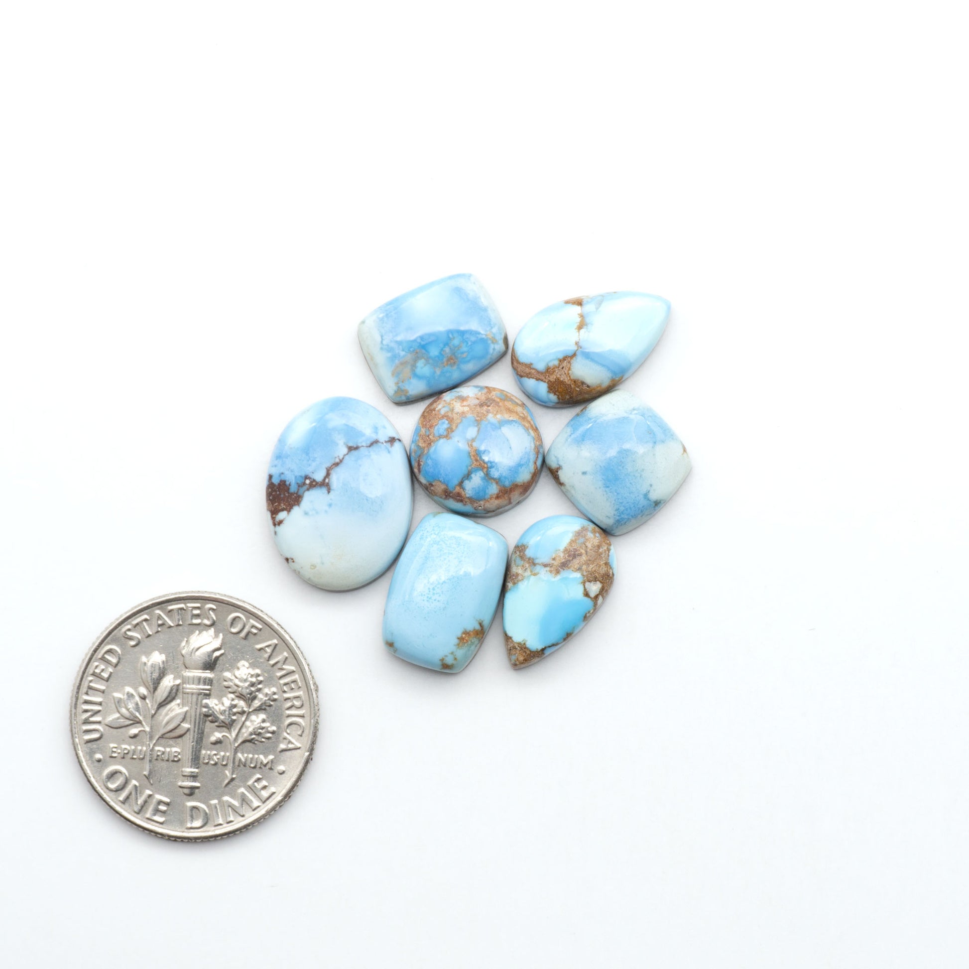 Golden Hills Turquoise cabochons, icy blue to lavender tones with chocolate matrix, polished stones on a white background with a US dime for scale