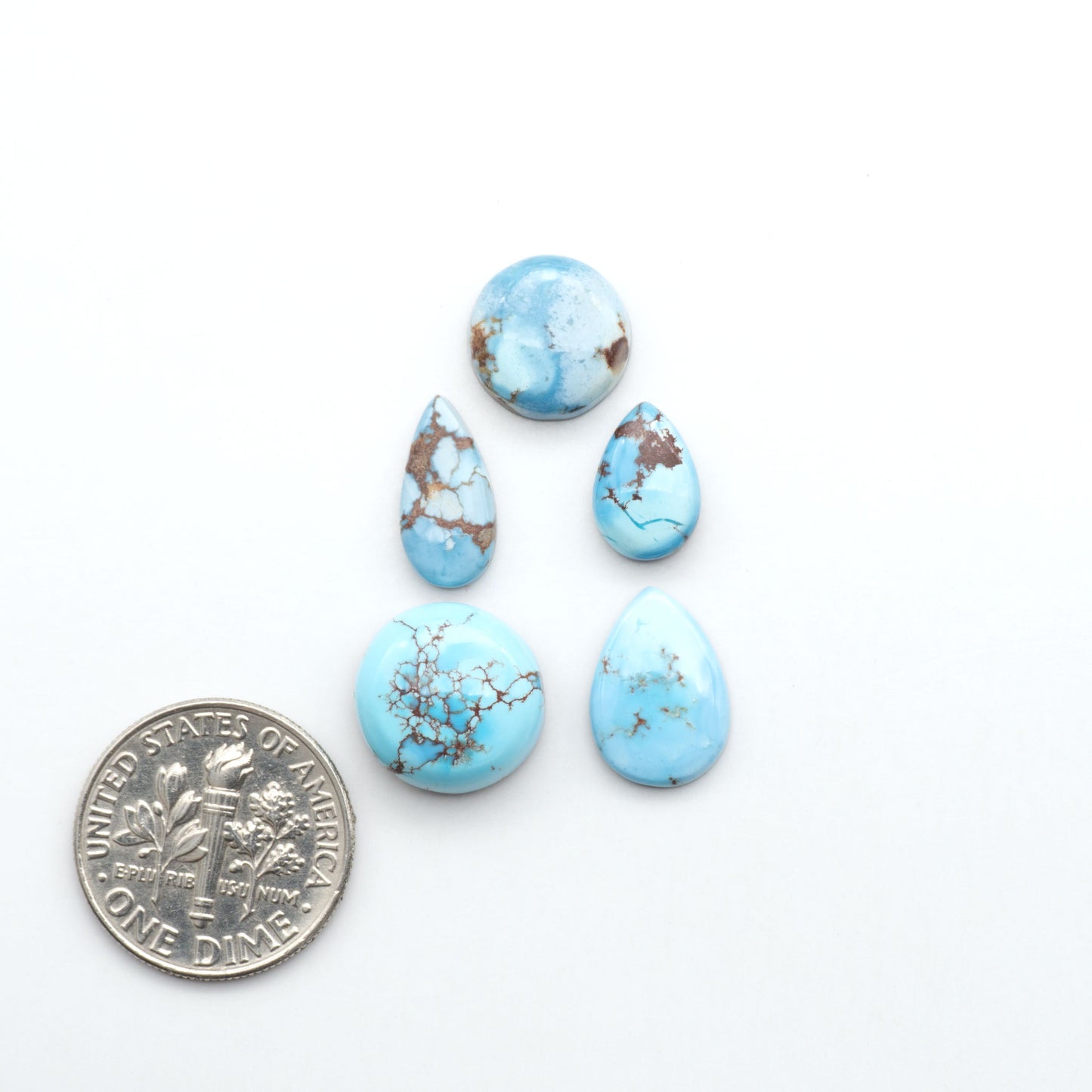 Golden Hills Turquoise cabochons, icy blue to lavender tones with chocolate matrix, polished stones on a white background with a US dime for scale