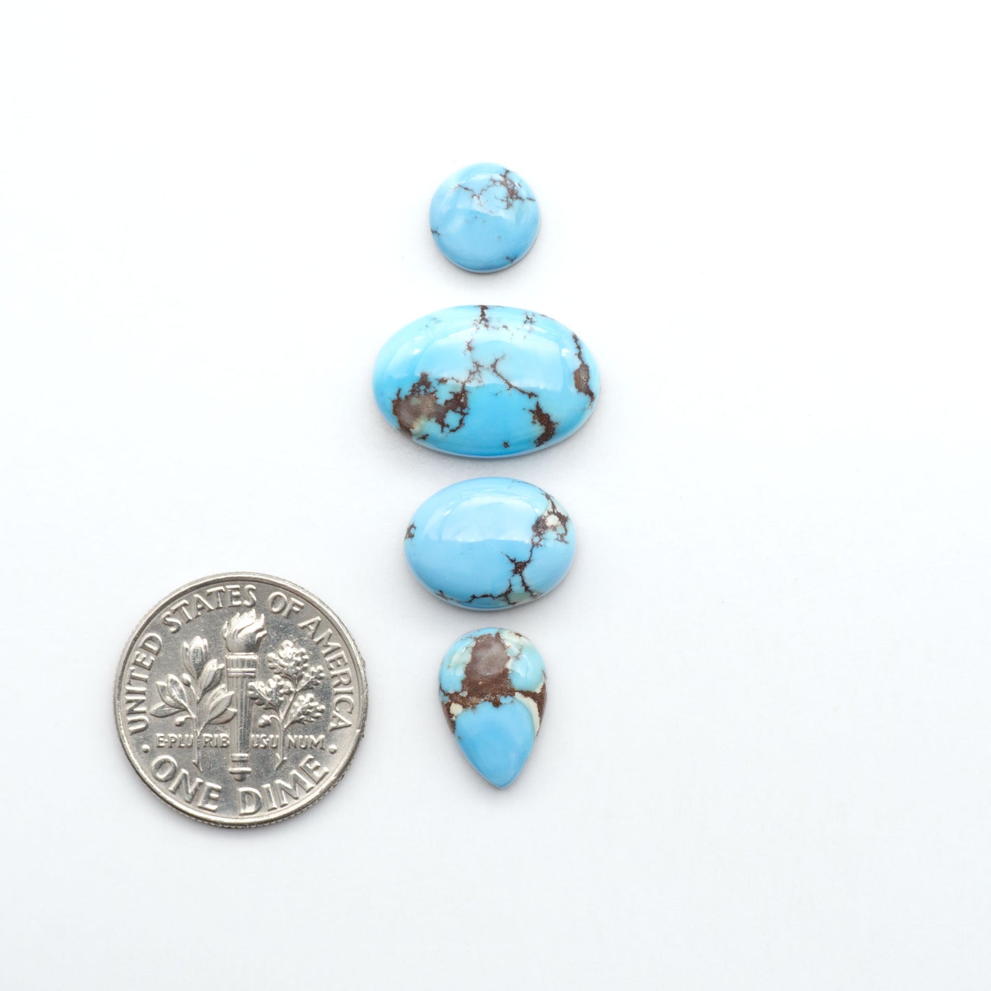 Golden Hills Turquoise cabochons, icy blue to lavender tones with chocolate matrix, polished stones on a white background with a US dime for scale