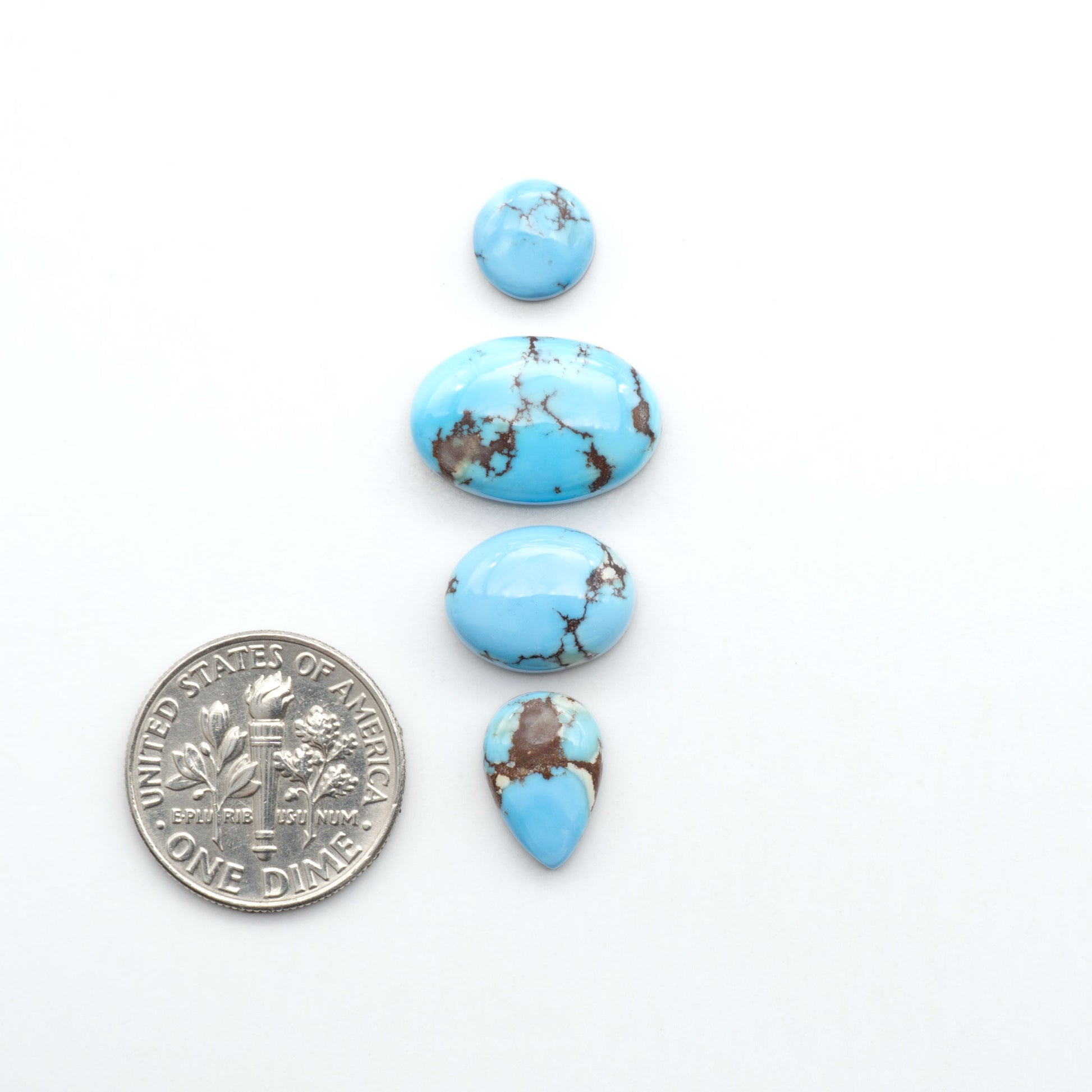 Golden Hills Turquoise cabochons, icy blue to lavender tones with chocolate matrix, polished stones on a white background with a US dime for scale