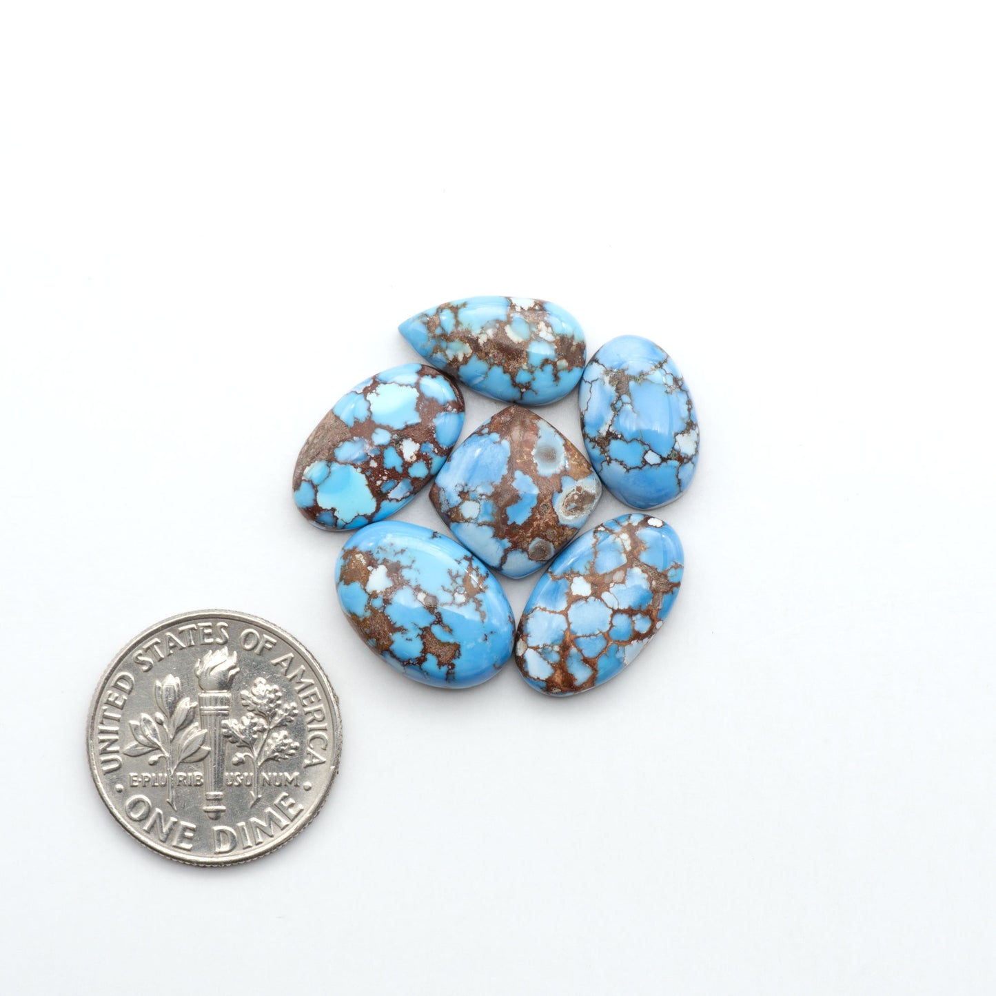Golden Hills Turquoise cabochons, icy blue to lavender tones with chocolate matrix, polished stones on a white background with a US dime for scale
