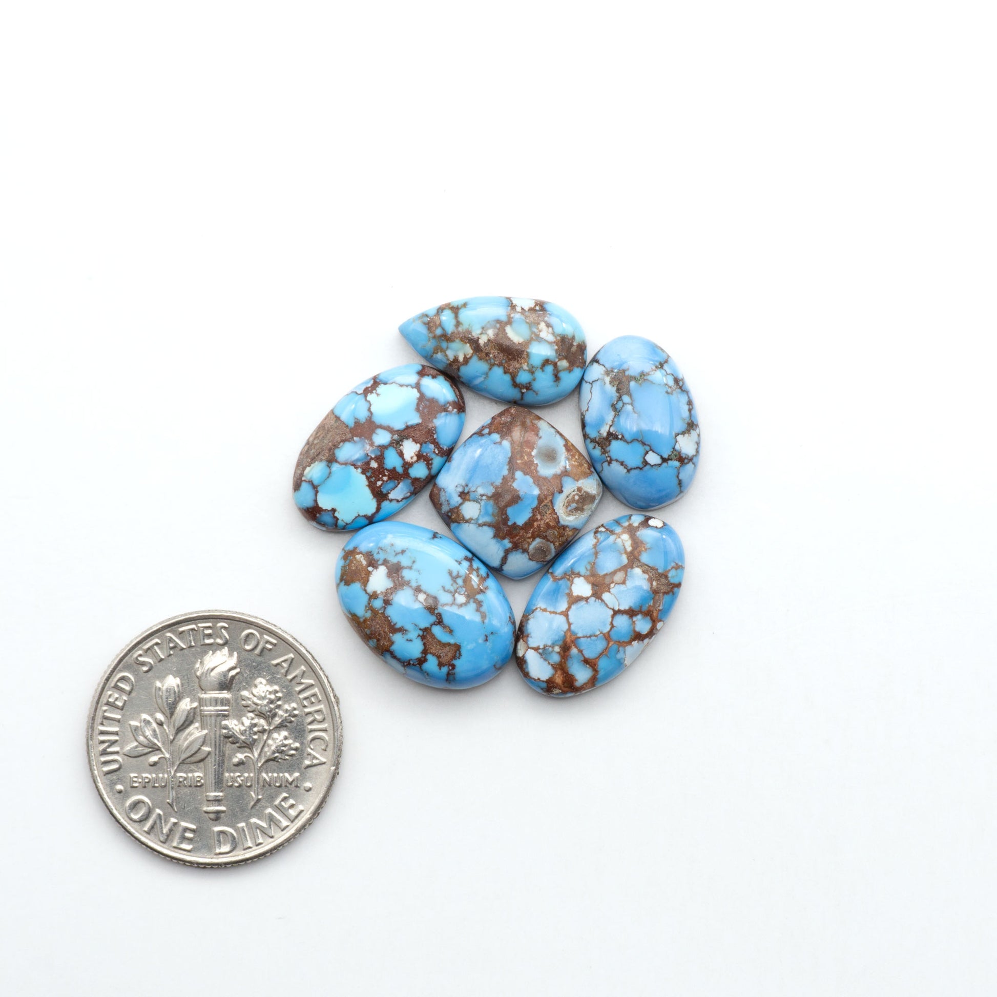 Golden Hills Turquoise cabochons, icy blue to lavender tones with chocolate matrix, polished stones on a white background with a US dime for scale