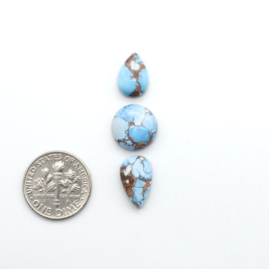 Golden Hills Turquoise cabochons, icy blue to lavender tones with chocolate matrix, polished stones on a white background with a US dime for scale