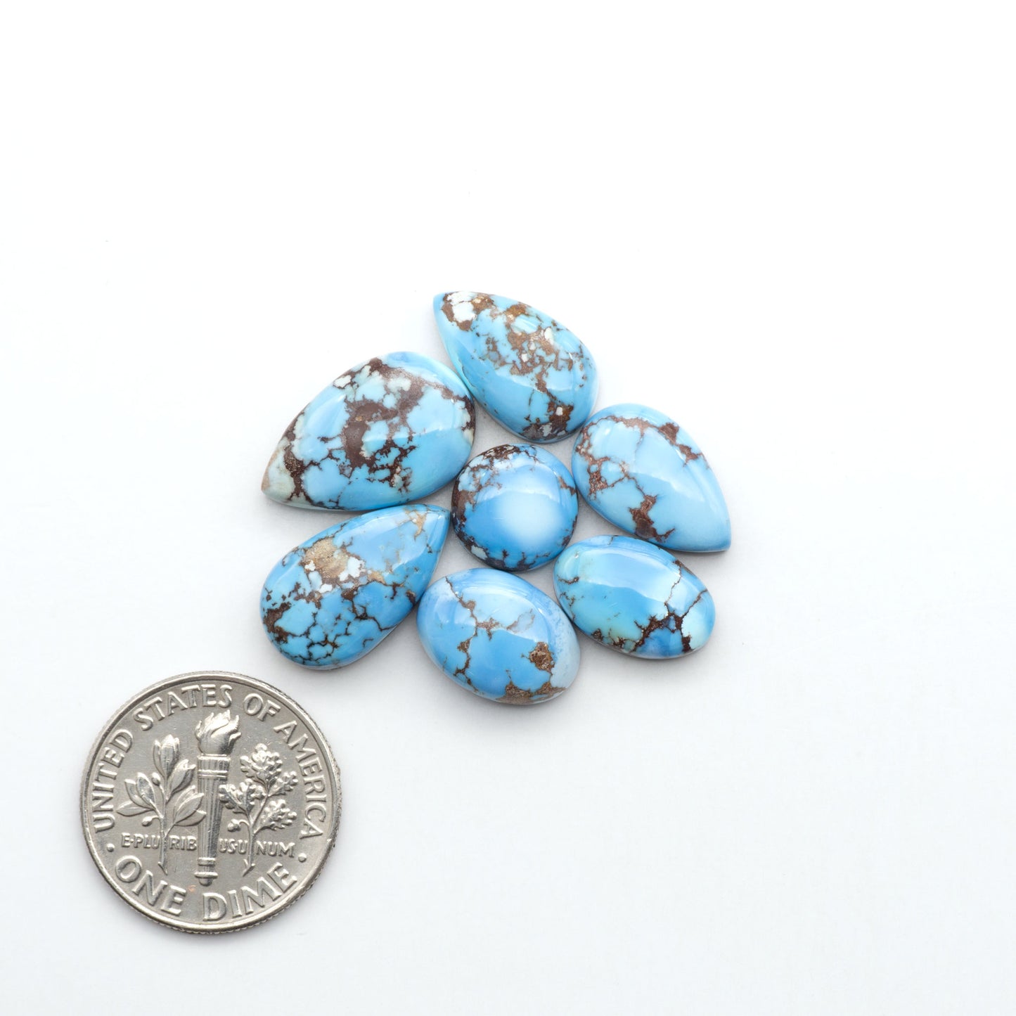 Golden Hills Turquoise cabochons, icy blue to lavender tones with chocolate matrix, polished stones on a white background with a US dime for scale