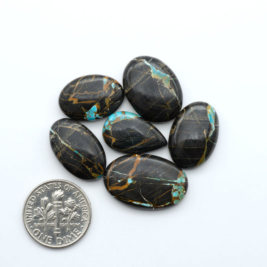 Black Jack turquoise cabochons, blue-green color with black matrix, polished stones on a white background with a US dime for scale