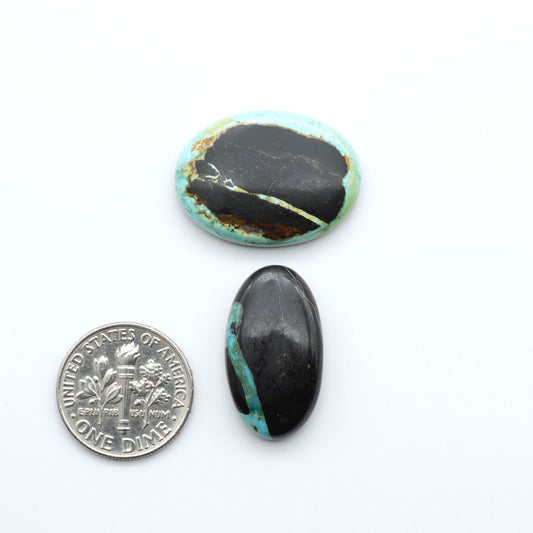 Black Jack turquoise cabochons, blue-green color with black matrix, polished stones on a white background with a US dime for scale