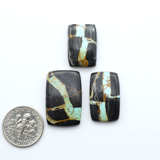 Black Jack turquoise cabochons, blue-green color with black matrix, polished stones on a white background with a US dime for scale