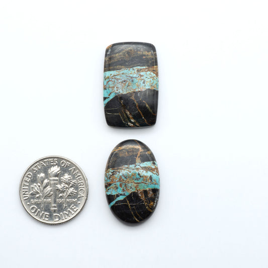 Black Jack turquoise cabochons, blue-green color with black matrix, polished stones on a white background with a US dime for scale