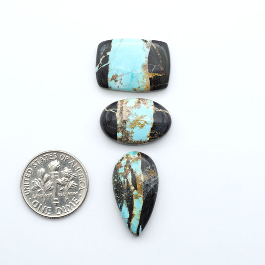 Black Jack turquoise cabochons, blue-green color with black matrix, polished stones on a white background with a US dime for scale