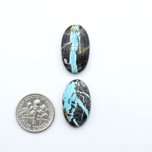 Black Jack turquoise cabochons, blue-green color with black matrix, polished stones on a white background with a US dime for scale