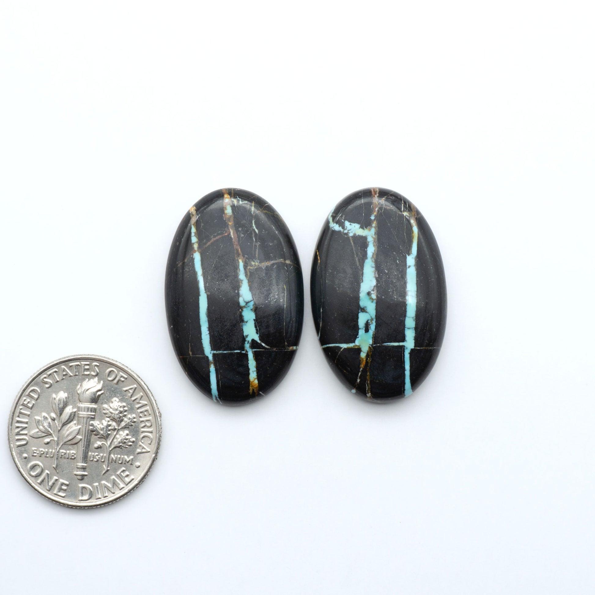 Black Jack turquoise cabochons, blue-green color with black matrix, polished stones on a white background with a US dime for scale