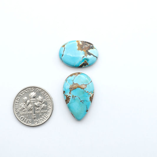 Black Jack turquoise cabochons, blue-green color with black matrix, polished stones on a white background with a US dime for scale