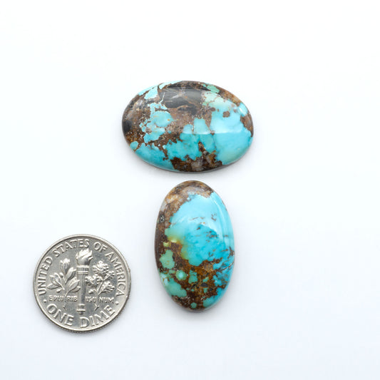 Black Jack turquoise cabochons, blue-green color with black matrix, polished stones on a white background with a US dime for scale