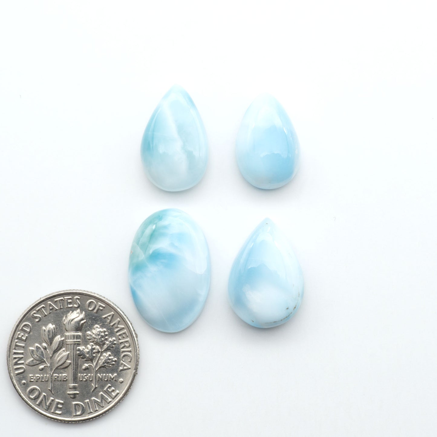Larimar stone cabochons, cut and polished, blue and white gemstones on a white background, with a US dime for scale