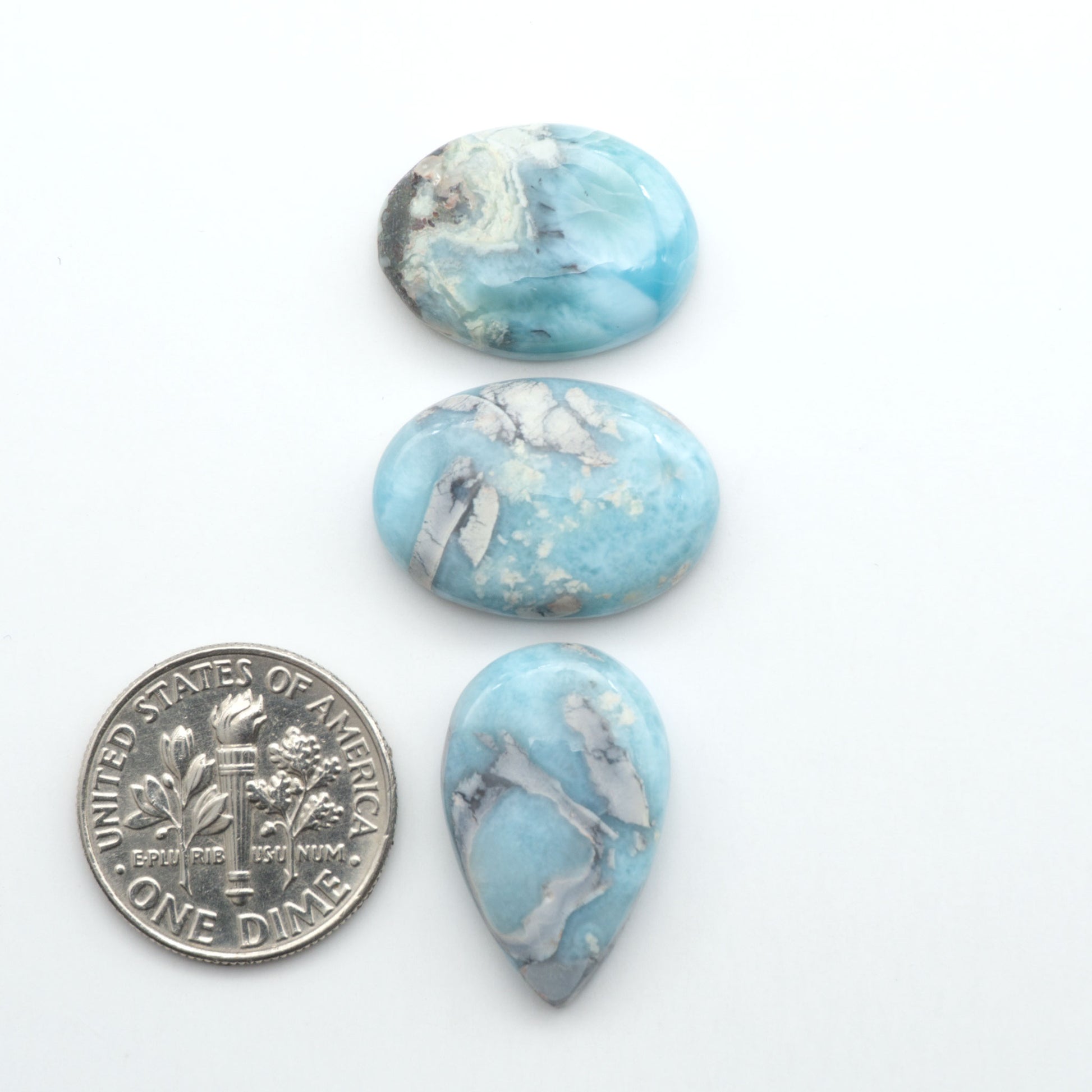 Larimar stone cabochons, cut and polished, blue and white gemstones on a white background, with a US dime for scale