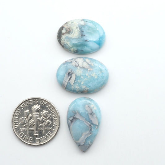 Larimar stone cabochons, cut and polished, blue and white gemstones on a white background, with a US dime for scale