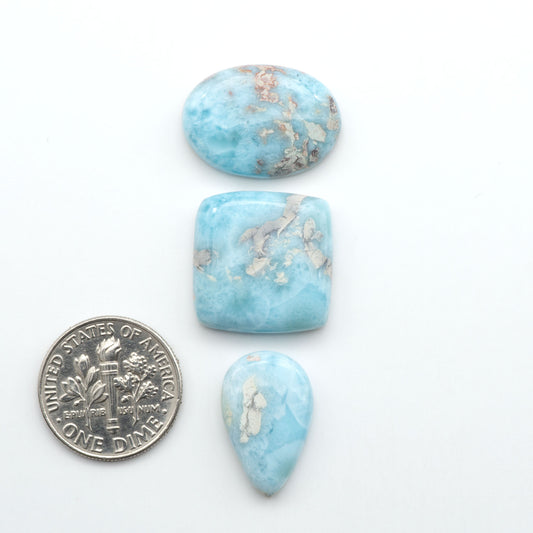 Larimar stone cabochons, cut and polished, blue and white gemstones on a white background, with a US dime for scale