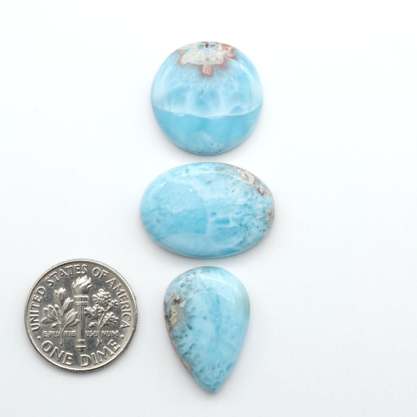 Larimar stone cabochons, cut and polished, blue and white gemstones on a white background, with a US dime for scale