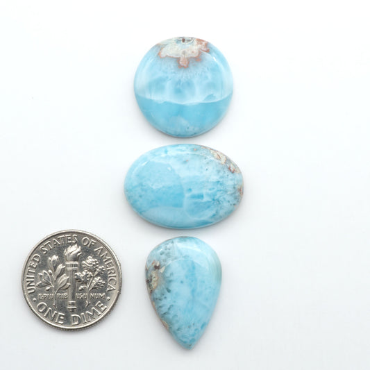 Larimar stone cabochons, cut and polished, blue and white gemstones on a white background, with a US dime for scale