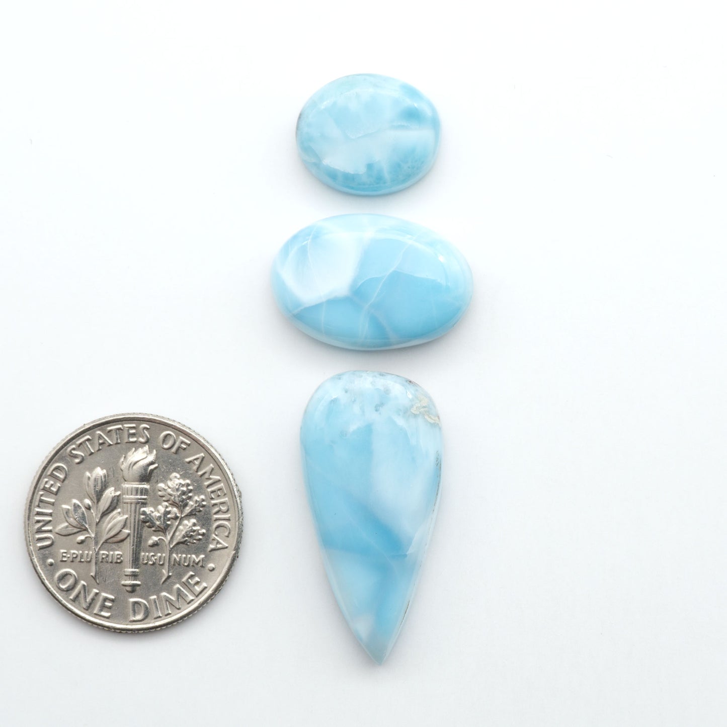 Larimar stone cabochons, cut and polished, blue and white gemstones on a white background, with a US dime for scale