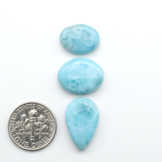 Larimar stone cabochons, cut and polished, blue and white gemstones on a white background, with a US dime for scale