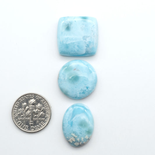 Larimar stone cabochons, cut and polished, blue and white gemstones on a white background, with a US dime for scale