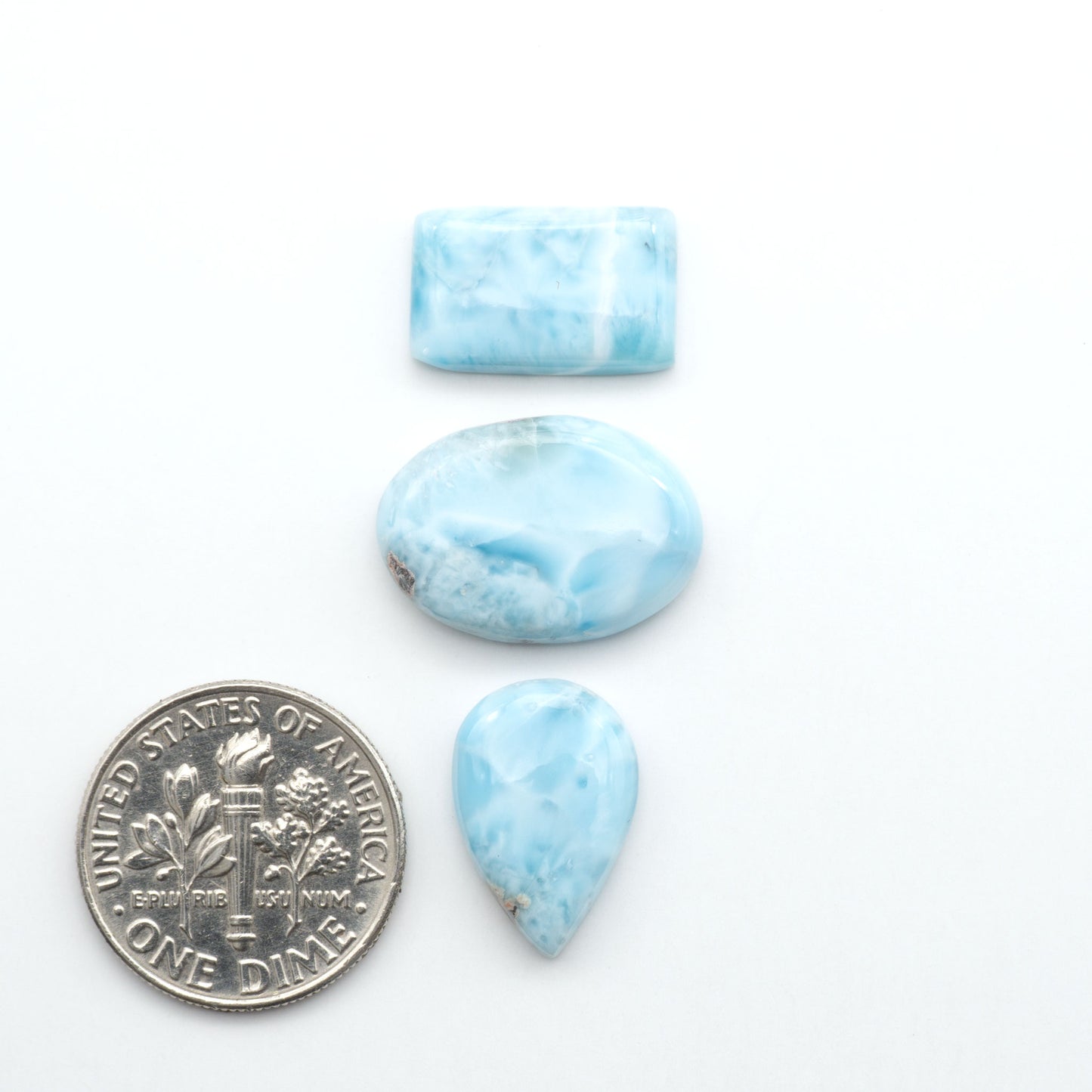Larimar stone cabochons, cut and polished, blue and white gemstones on a white background, with a US dime for scale
