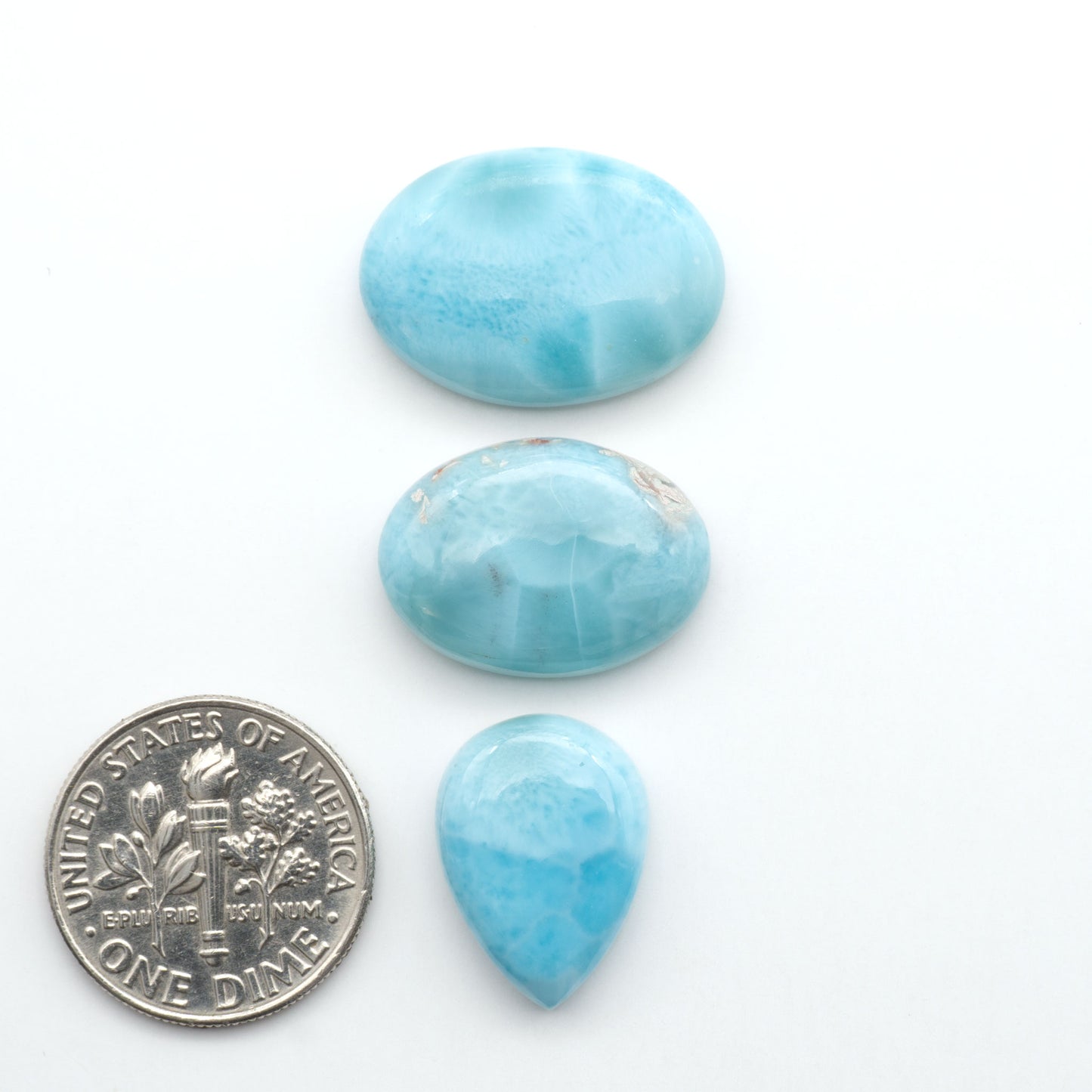 Larimar stone cabochons, cut and polished, blue and white gemstones on a white background, with a US dime for scale