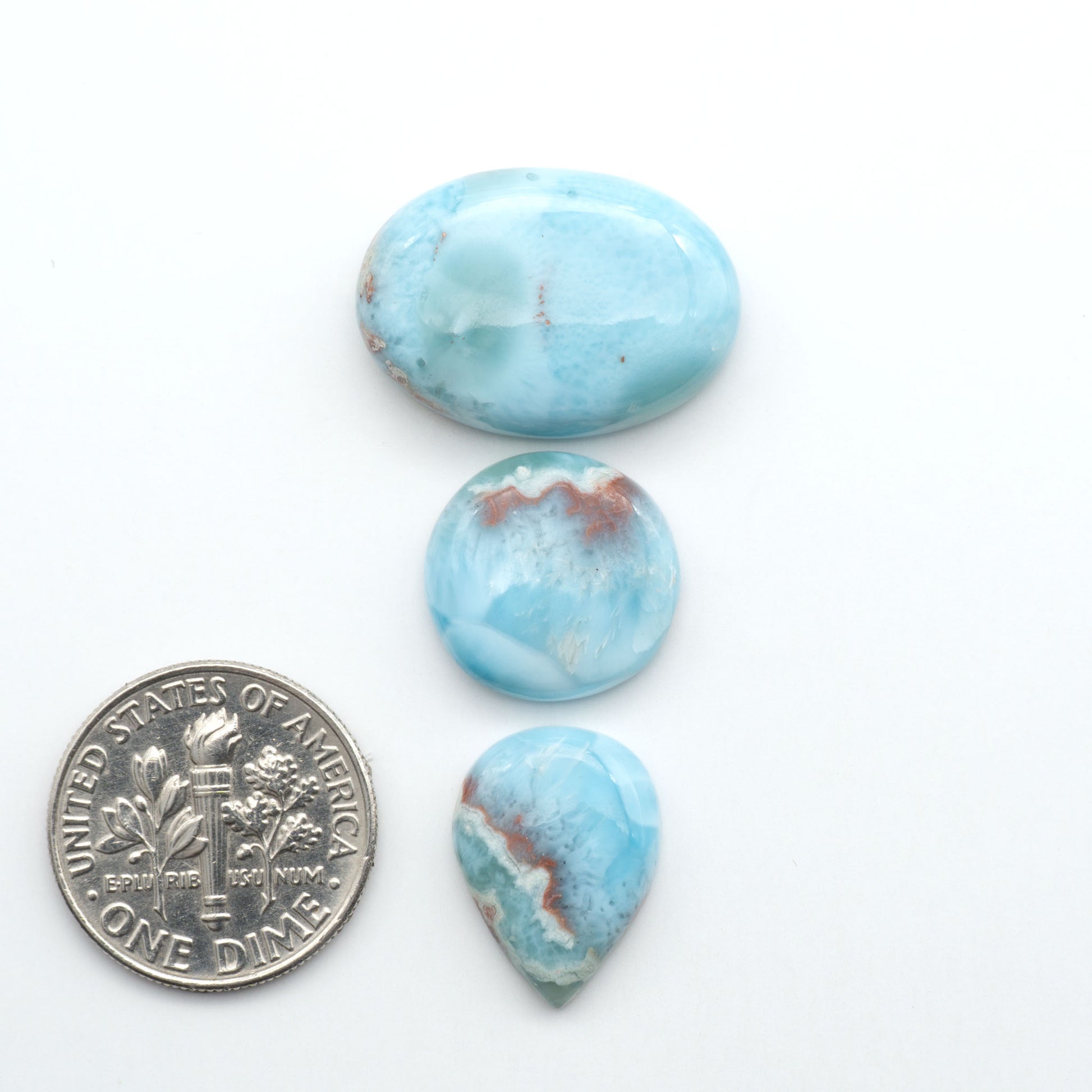 Larimar stone cabochons, cut and polished, blue and white gemstones on a white background, with a US dime for scale